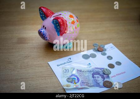 Piggy bank con bolletta del gas, banconote inglesi £20 e monete come razzo bollette del carburante Foto Stock