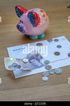 Piggy bank con bolletta del gas, banconote inglesi £20 e monete come razzo bollette del carburante Foto Stock