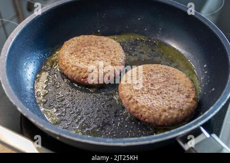 Due hamburger polpette carne hamburger sfrigolando in una padella calda con grasso e olio come deliziosi hamburger di carne barbecue Selfmade polpette come insalubre fast food pranzo Foto Stock