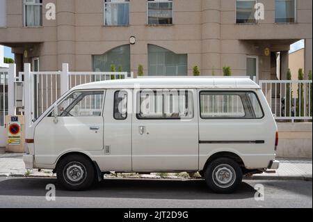 Una vista laterale di primo piano di un vecchio furgone bianco Nissan Vanette parcheggiato sulla strada di fronte ad un edificio Foto Stock