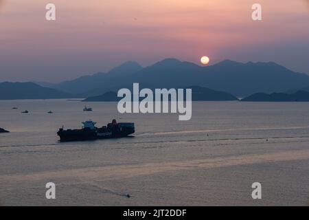 Un bel cielo rosa tramonto sul mare con una grande nave da carico e sagome di montagne, canale di Lamma, Hong Kong Foto Stock