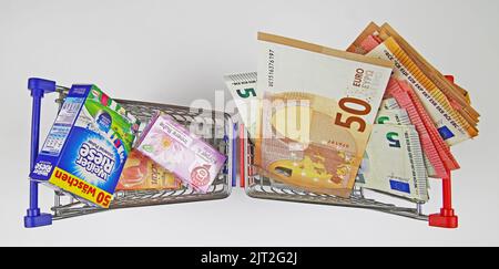 Viersen, Germania - Luglio 9. 2022: Primo piano di due modelli di carrelli con prodotti di marca e un sacco di banconote in euro in contanti Foto Stock