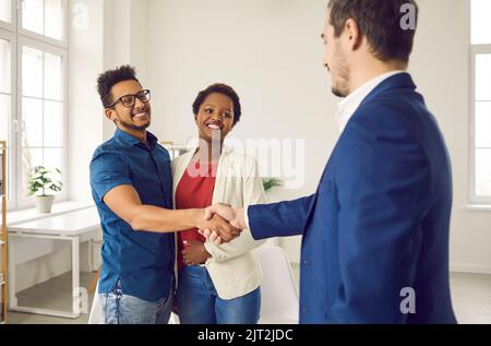 Felice coppia nera scambiando handshakes con un agente immobiliare o un mediatore di prestito Foto Stock