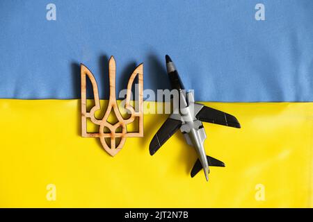 Un aereo giocattolo per bambini giace sulle bandiere nazionali dell'Ucraina e uno stemma di legno, la guerra in Ucraina, un cielo chiuso Foto Stock