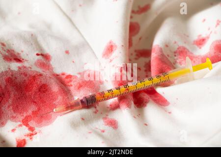 Macchie di sangue su un abito bianco e una siringa, trattamento e medicina Foto Stock