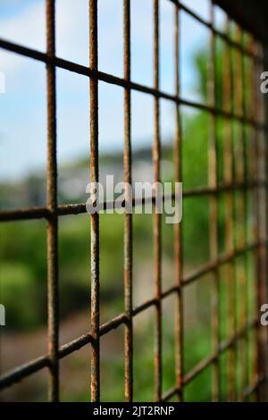 Vista sulla città tra le arrugginite barre di ferro e le maglie di ferro Foto Stock