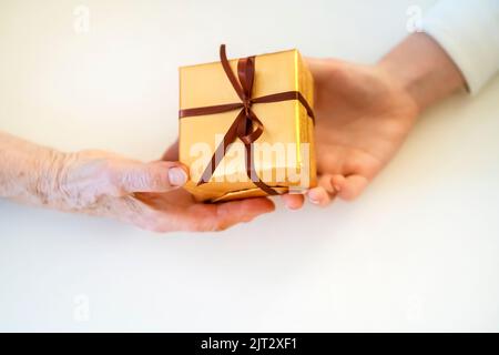 Le mani femminili tengono e danno un regalo imballato piacevole. Foto Stock