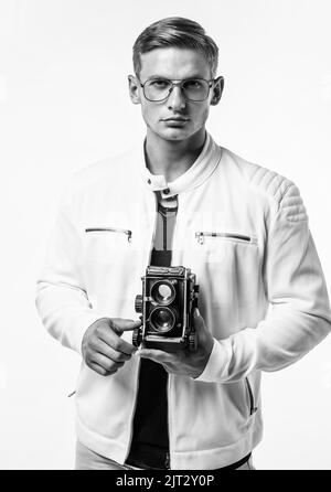 Il desiderio incontra un nuovo hobby. Bel ragazzo tenere retro fotocamera isolato su bianco. I giovani fotografi indossano occhiali in stile casual. Attrezzatura fotografica Foto Stock