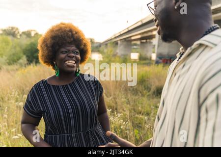 Sorridente coppia etnica con pelle scura e dritta, con una rilassante serata estiva, parlando, ridendo e passeggiando nella natura vicino al fiume. Foto di alta qualità Foto Stock