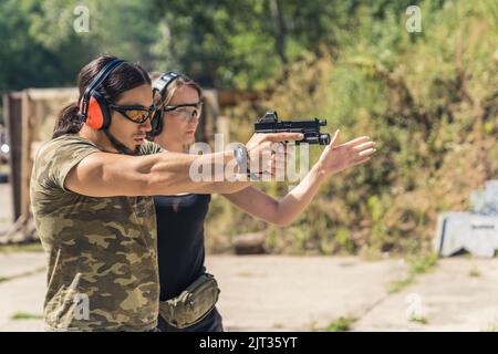 La sicurezza prima di tutto. Due persone caucasiche in un campo di tiro indossando occhiali protettivi e cuffie. Uomo muscolare che punta con una pistola con collimatore. Istruttore femminile che lo corregge. Foto di alta qualità Foto Stock