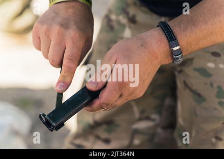 Concetto di sparatoria. Due mani di un uomo caucasico irriconoscibile in pantaloni moro che mostrano una parte nera di una pistola o di un fucile alla fotocamera. Primo piano all'aperto. Foto di alta qualità Foto Stock