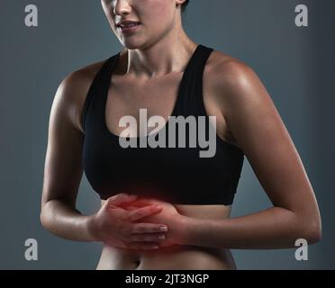 La disidratazione ha comunemente un ruolo nello stomaco e nei dolori addominali. Studio shot di una giovane donna sportiva che sperimenta mal di stomaco. Foto Stock