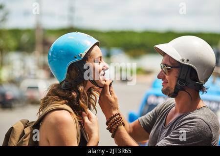 L'amore è sempre lì per dare una mano d'aiuto. Un giovane felice che aiuta la sua ragazza a indossare un casco per moto in strada. Foto Stock