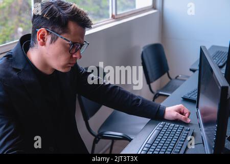 Lavoratore di ufficio che guarda il suo computer infastidito. Lavoratore che guarda il computer alla sua scrivania in casa sua. Uomo elegante con occhiali in ufficio. Foto di alta qualità Foto Stock