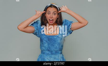 Bella donna divertente in vestito rendendo divertenti espressioni facciali sciocco e grimacing, imbrogliando intorno, mostrando la lingua. Ragazza donna elegante adulto isolato da solo su sfondo grigio studio al coperto Foto Stock