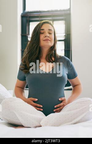 Mantenere il bambino in buona salute. Una giovane donna incinta che fa yoga mentre si siede sul suo letto. Foto Stock