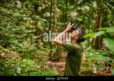 La macchina fotografica vede che cosa i suoi occhi cant. Un giovane fotografo che esplora una giungla tropicale. Foto Stock