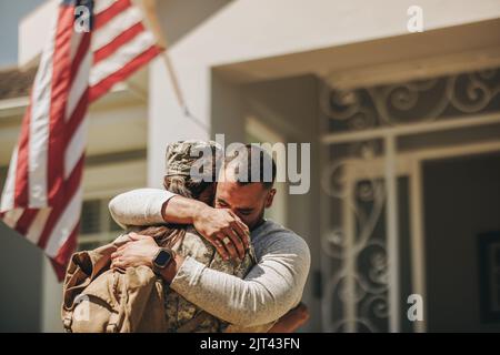 Emotivo ritorno a casa militare. Soldato femminile che abbraccia il marito dopo il ritorno a casa dall'esercito. Americano servicewoman riunendosi con il suo husba Foto Stock