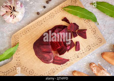 Barbabietole rosse a fette su un tagliere di legno con aglio, cipolla e spezie - preparazione di verdure fermentate Foto Stock