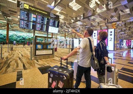 SINGAPORE - CIRCA GENNAIO 2020: Passeggeri che guardano i monitor degli orari dei voli all'Aeroporto Changi di Singapore. Foto Stock