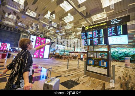 SINGAPORE - CIRCA GENNAIO 2020: Passeggeri che guardano i monitor degli orari dei voli all'Aeroporto Changi di Singapore. Foto Stock