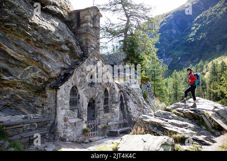 Donna escursionista di fronte alla cappella di Maria Schnee vicino a Innergschlöß nella valle del Glossal, Parco Nazionale degli alti Tauri, Tirolo orientale, Austria Foto Stock
