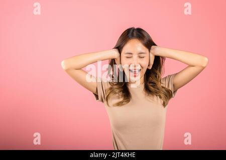 Ritratto asiatico bella giovane donna hanno orecchie strette con mani palme e occhi stretti, studio shot isolato su sfondo rosa, Thai femmina orecchio di copertura Foto Stock