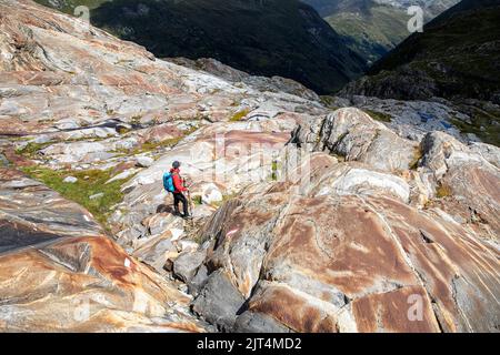 Donna che si arrampica su rocce colorate su una morena del ghiacciaio su un bellissimo sentiero del ghiacciaio Innergschlöss fino al ghiacciaio di Schlatenkees, Tirolo orientale, Austria Foto Stock