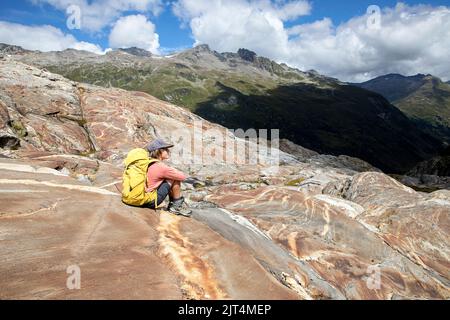 Ragazzo seduto su rocce colorate su una morena del ghiacciaio su un bellissimo sentiero del ghiacciaio Innergschlöss fino al ghiacciaio di Schlatenkees, Tirolo orientale, Austria Foto Stock