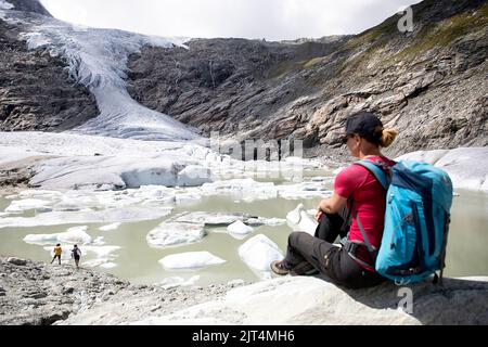 Donna escursionista che guarda il ghiacciaio schlatenkees, il lago del ghiacciaio e la morena del ghiacciaio nel gruppo montuoso di Venediger, parco Hohe tauern, Tirolo orientale, Austria Foto Stock