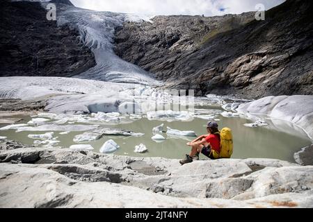 Ragazzo che si siede e guarda il ghiacciaio dello schlatenkees, il lago del ghiacciaio e la morena del ghiacciaio nel gruppo montuoso di Venediger, Tirolo Orientale, Austria Foto Stock