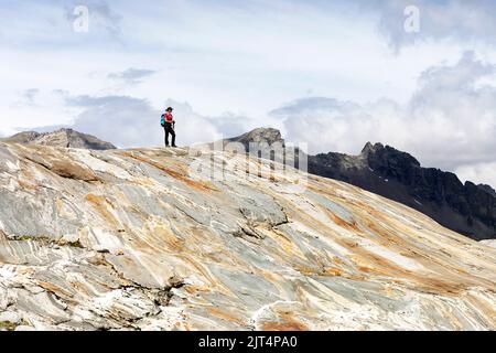 Donna che si arrampica su rocce colorate su una morena del ghiacciaio su un bellissimo sentiero del ghiacciaio Innergschlöss fino al ghiacciaio di Schlatenkees, Tirolo orientale, Austria Foto Stock