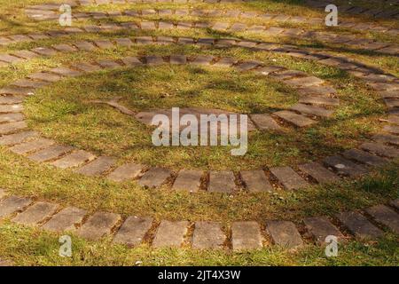 Una vista di un sentiero serpente nel giardino Brandon Country Park, Suffolk, che mostra i mattoni distanziati affondati nel prato, erba. Foto Stock