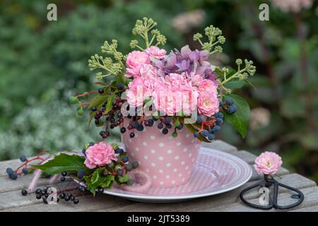 bouquet di rose rosa, fiori di ortensia, bacche di sambuco, bacche di vino selvatico e edera fruttata in tazza Foto Stock