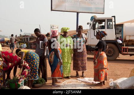 Zorzor Town Centre, Contea di Lofa. Liberia, Africa. Riso versato sulla strada e wome vendere ananas. Donne africane elegantemente vestite. Foto Stock