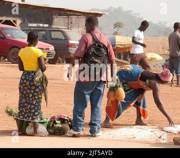 Vendita di ananas, Zorzor Town Centre, Contea di Lofa. Liberia, Africa - il riso versato sulla strada viene raccolto dalla donna Foto Stock