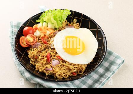 Indomie Goreng o mie Goreng, indonesiano popolare Instant Noodle. Servito con uovo di lato soleggiato, pomodoro, cetriolo. Foto Stock