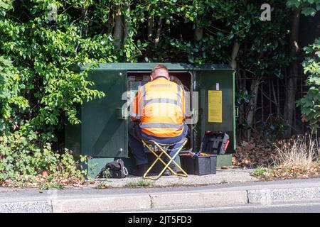 Ingegnere Openreach che lavora in una scatola verde con cavi di comunicazione, mantenendo la rete telefonica e a banda larga, Regno Unito Foto Stock