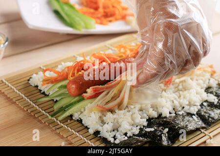 Primo piano femminile coreana Gimbap, riso coreano con Sausace, Kyuri, carota e bastone. Preparazione dettagliata cottura Foto Stock
