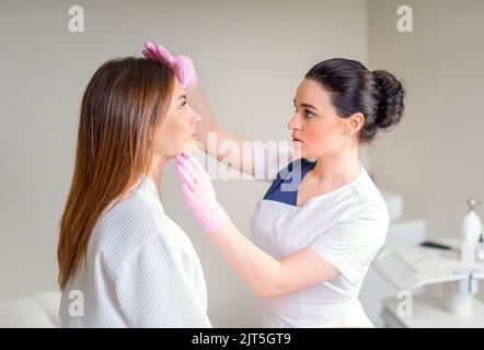 Professional cosmetico esaminando la pelle del viso della ragazza in clinica di Cosmetologia estetica Foto Stock