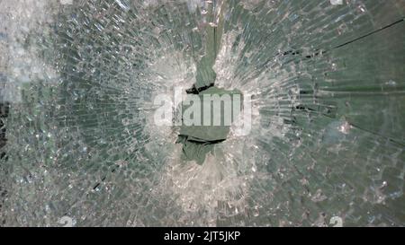 Vetro teso finestra rotta con un foro al centro da scheggia di esplosione. Vetro frantumato. Astratto sfocato sfocato trama di vetro rotto backg Foto Stock