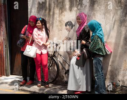 Posa intorno Street Art, George Town, Penang, Malesia, Asia. Giovani donne musulmane che si divertono e si divertono. Street art è molto comune in G Foto Stock