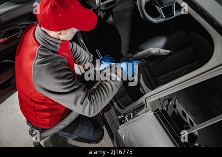 Addetto al servizio automobilistico caucasico addetto alla pulizia degli interni dell'auto. Aspirazione dei sedili. Tema dell'industria dei trasporti. Foto Stock