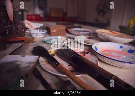 Pennelli di vernice di un artista cinese in piedi sul tavolo in un piatto con altre pitture ad olio intorno Foto Stock