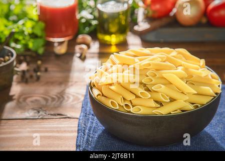 Recipiente per pasta di penne crude con ingredienti freschi su fondo rustico in legno. Foto Stock