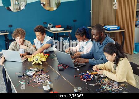 Vista ad angolo alto in un gruppo diversificato di bambini con insegnanti maschi che costruisce robot durante la classe di ingegneria a scuola Foto Stock