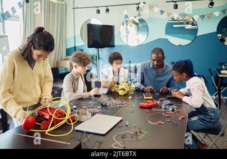 Gruppo eterogeneo di bambini che costruisce robot con insegnanti maschi che aiutano durante la lezione di ingegneria a scuola Foto Stock