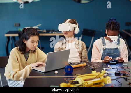 Un gruppo eterogeneo di bambini che costruisce robot in classe ingegneristica e utilizza la tecnologia VR Foto Stock