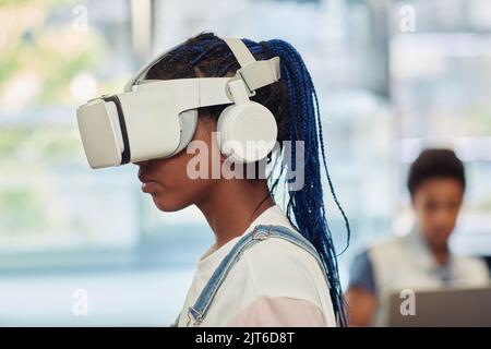 Ritratto con vista laterale di una ragazza adolescente nera che utilizza la tecnologia VR nella classe di ingegneria Foto Stock