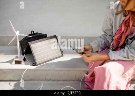 Donna carica il telefono da un pannello solare portatile Foto Stock